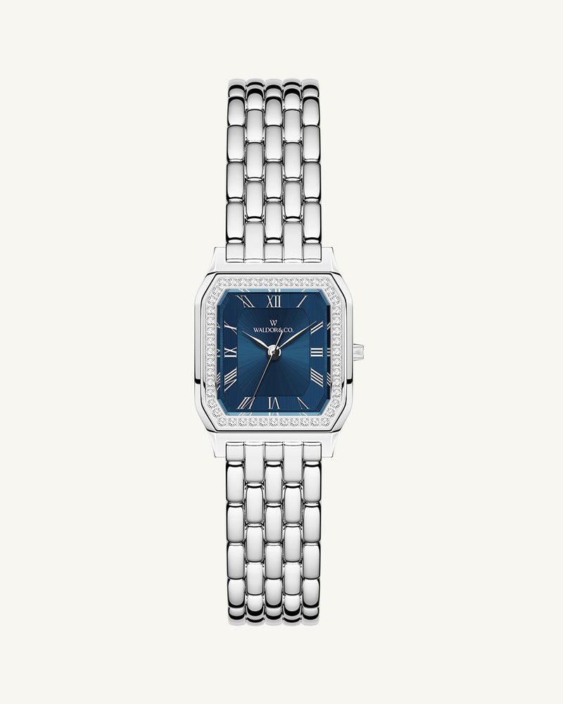 A square womens watch in Rhodium-plated 316L stainless steel from Waldor & Co. with dark blue dial. Bezel with premium crystals. Diamond Cut Sapphire Crystal glass dial. Seiko movement. The model is Eternal 22 Bellagio Pavè.