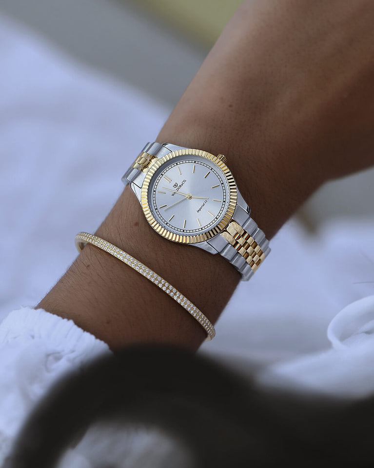 A round womens watch in silver and 22k gold from Waldor & Co. with silver sunray dial and a second hand. Seiko movement. The model is Imperial 32 Positano 32mm.